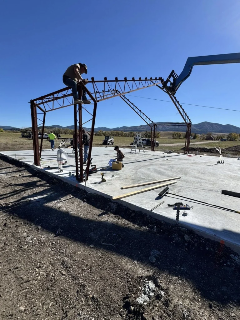Workers assembling a steel frame structure on top of a newly poured commercial concrete slab.