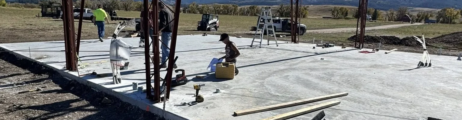 Workers assembling a steel frame structure on top of a newly poured commercial concrete slab.